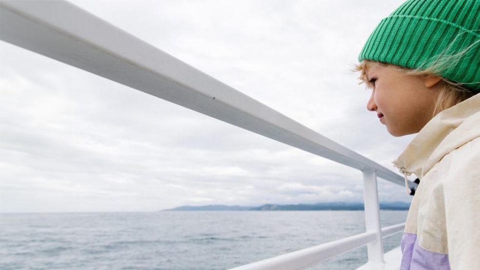 A girl standing on the ferry in a windy weather. She wants to see the whale in the sea