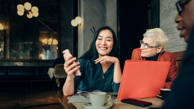 lady showing colleagues something amusing on her mobile while working
