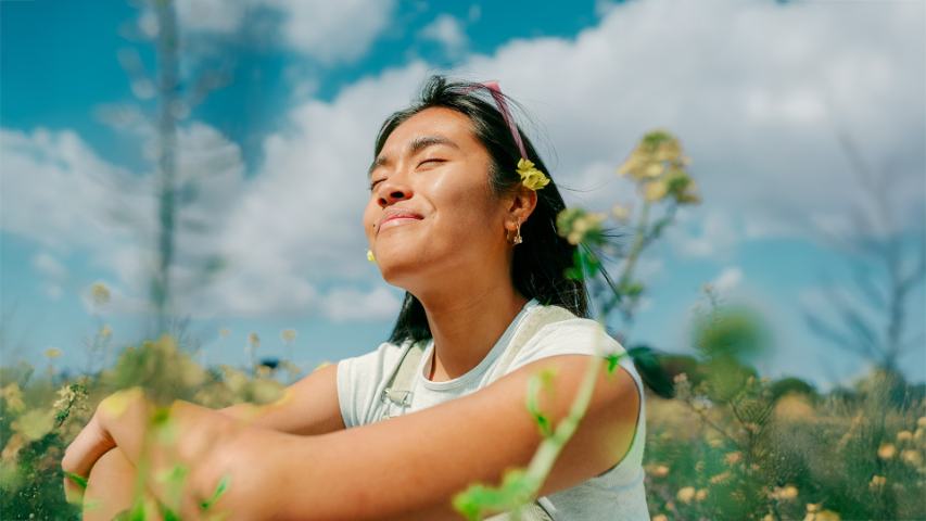 smiling woman sitting in field with yellow flowers
