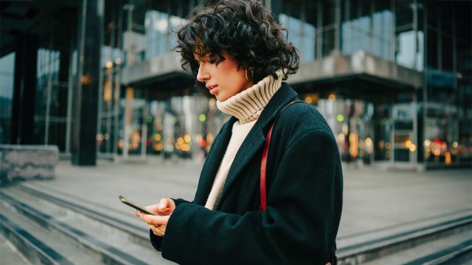 young woman in a winter jumper and jacket looking at her phone walking in the city