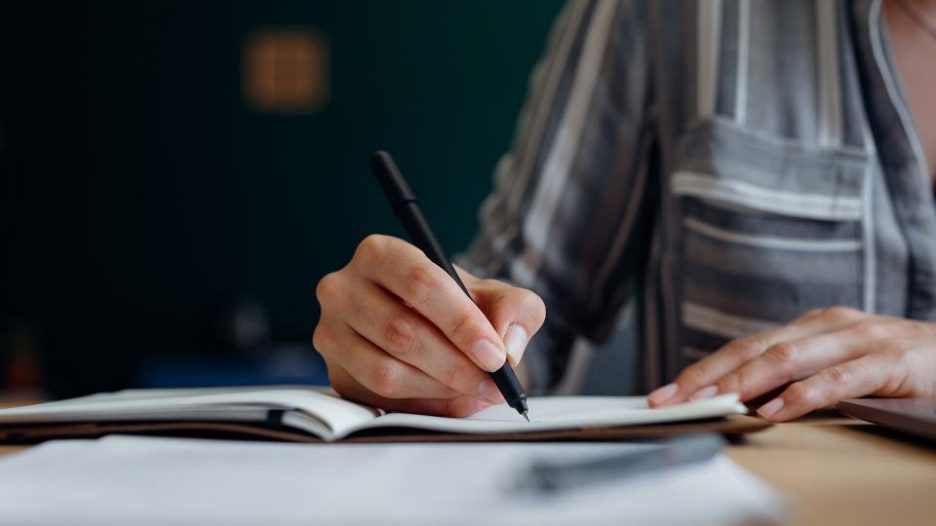 close up of a female hand writing in a notebook using a black pen